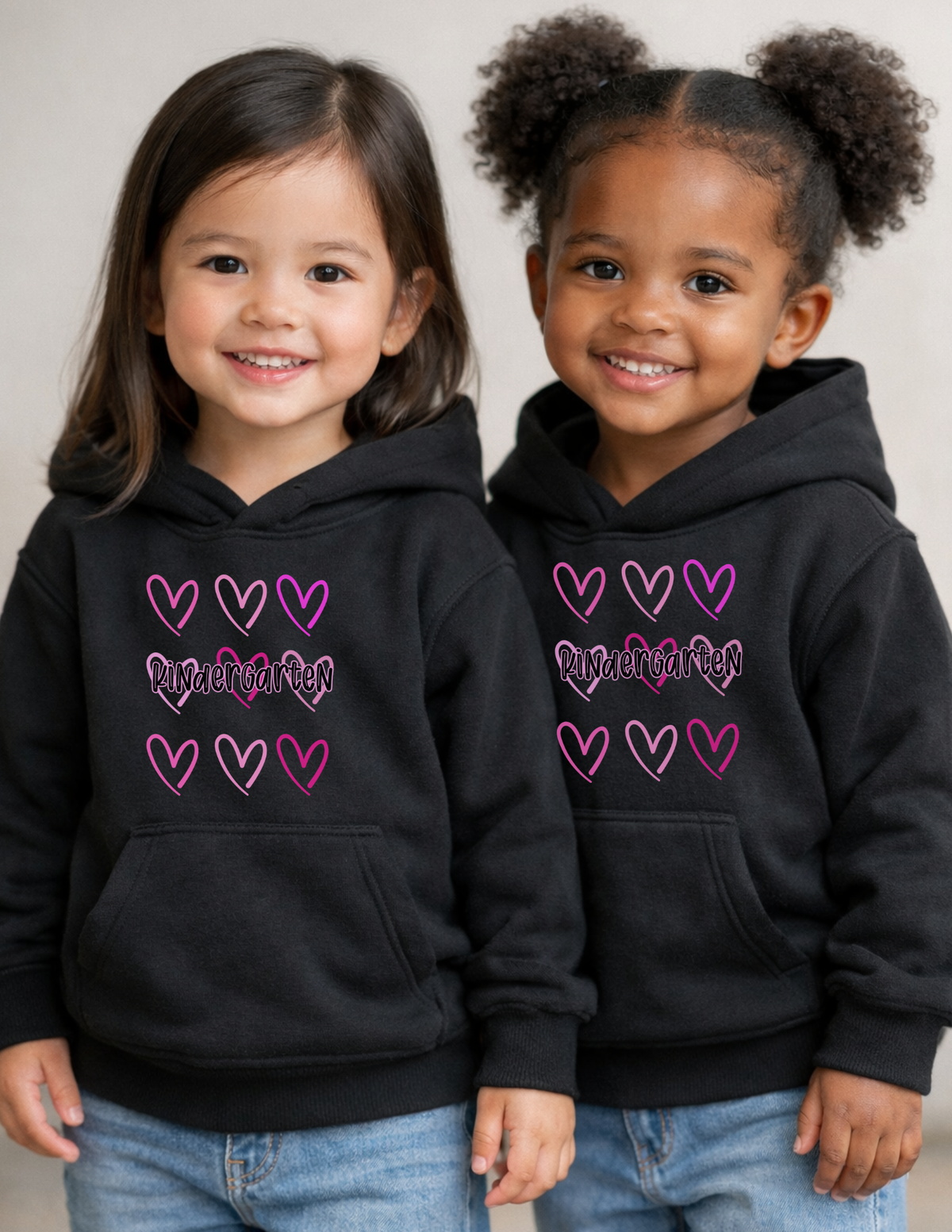 Two children wearing black hoodies with pink hearts and text.